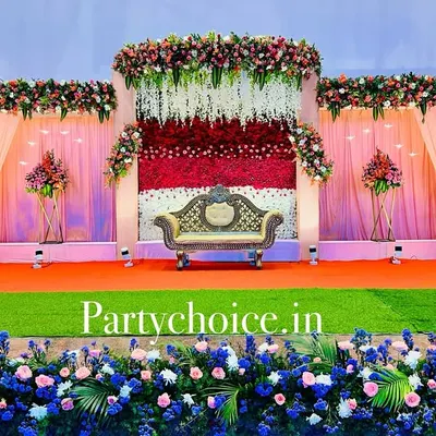 This is a grand outdoor reception stage we built. The design features a multi-layered backdrop with pink drapes, a central wall of red and white flowers, and extensive floral borders, creating a lavish and picturesque setting.