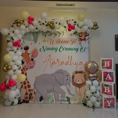 A cute jungle animal theme for a naming ceremony. The backdrop features a giraffe, elephant, and lion, framed by a balloon arch and complemented by "BABY" blocks for a complete photo-ready setup.
