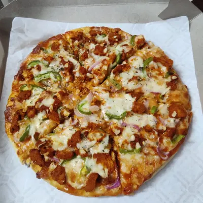 A full view of my homemade chicken pizza, sliced and ready to eat. It's packed with toppings like seasoned chicken, crunchy green capsicum, and onions, all covered in melted mozzarella cheese.