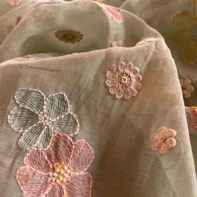 This close-up shows the exquisite detail of 3D floral embroidery on a soft Mul Chanderi base. The mix of pink and blue threads with pearl centers makes this fabric a piece of art, ready to be turned into a bespoke kurta.