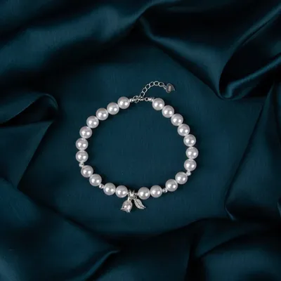A delicate silver and pearl bracelet, shot on a dark teal satin background to create a feeling of elegance and luxury.