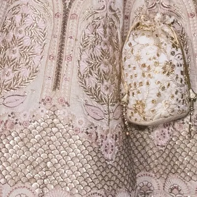 A close-up of the intricate floral and lattice embroidery on our ivory bridal lehenga. The matching potli bag also features the same detailed craftsmanship.