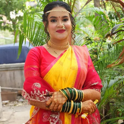 A classic Maharashtrian bride in a vibrant yellow and red saree. Her makeup is traditionally elegant with a focus on defined eyes, a small bindi, and a radiant complexion.