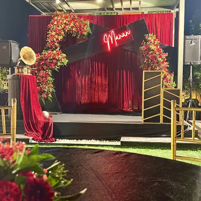 A glamorous stage setup for a musical night. The decor featured a custom neon sign with the host's name, a rich red velvet backdrop, and dramatic floral arrangements.