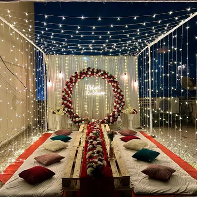 A full view of our signature fairy light canopy setup on a terrace. The low pallet table, colorful cushions, and floral centerpiece create a perfect setting for a private party, mehndi night, or bachelorette.