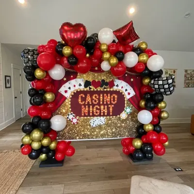 A 'Casino Night' themed party backdrop. This setup features a sequined gold curtain, a balloon arch in red, black, and gold, and themed foil balloons like hearts, diamonds, and playing cards.