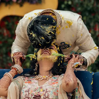 A playful and candid moment where the groom lovingly applies haldi to the bride's face. Their laughter and intimacy make this a standout shot from the pre-wedding festivities.