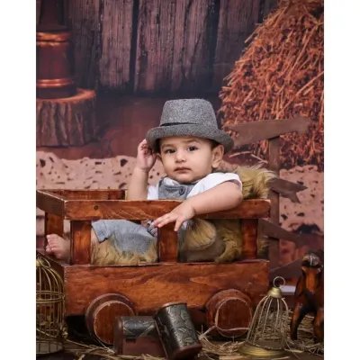 This dapper little boy tips his hat, adding a touch of old-school charm to his vintage photoshoot. The rustic barn backdrop and wooden cart create a timeless, classic feel.
