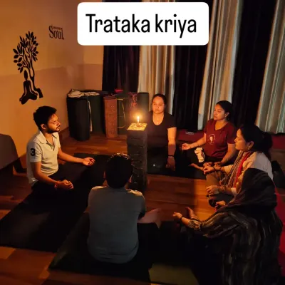 A group of students is fully absorbed in the practice of Trataka Kriya. The candle flame provides a single point of focus, helping to still the fluctuations of the mind.