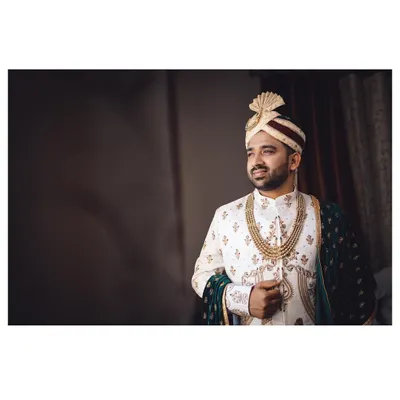 A quiet moment of preparation for the groom. This portrait captures him looking thoughtful and handsome in his wedding sherwani just before the ceremony begins.