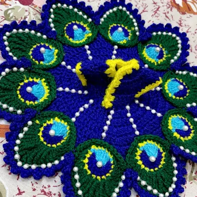 A flat-lay view of the classic Mor Pankh poshak, showing the intricate crochet work. The design features peacock feather patterns in royal blue and deep green, with each 'eye' of the feather highlighted by a white pearl.