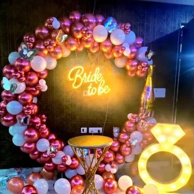 This is my most popular bride-to-be party setup, featuring a rose gold and white balloon ring, a "Bride to be" neon sign, and a light-up diamond ring prop. A small stool is included for guests to sit and take photos.