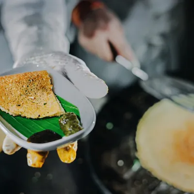The sizzle of a fresh dosa being made is a highlight at any event. A chef serves a mini dosa on a banana leaf, offering a bite-sized piece of South Indian culinary art.