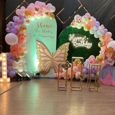 A dreamy butterfly and princess theme for Sharvi's first birthday. This elaborate setup features a large butterfly cutout, a Princess Sofia prop, pastel balloon arches, and a light-up number '1' to create a fairytale setting.