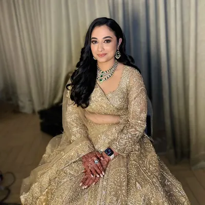 A full-length shot of my beautiful reception bride, Neha. She looks absolutely regal in her golden lehenga, with makeup that features soft golden eyes and a flawless base, complemented by elegant side-swept waves.
