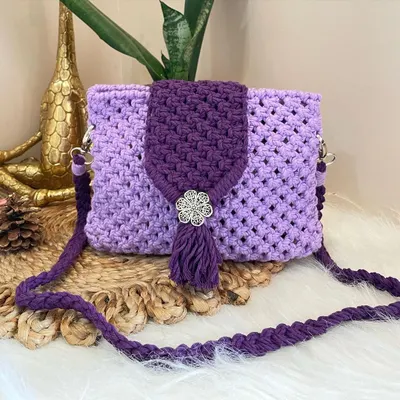 Embrace the magic of purple with this enchanting sling bag. It features a dark purple flap with a decorative metal flower and tassel, set against a lighter lavender body for a beautiful two-tone effect.