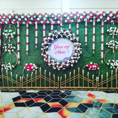 A creative name reveal idea for a naming ceremony. A floral wreath with a "Guess my Name?" sign is the centerpiece of this beautiful greenery backdrop.