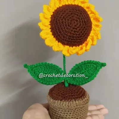 Our standard-sized crochet sunflower in a pot, held to show its scale. This piece is perfect for a desk or shelf, adding a touch of handmade sunshine to your decor.