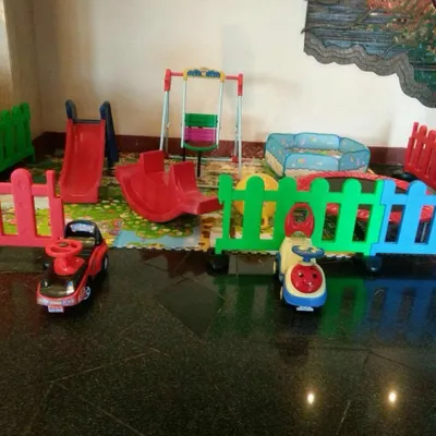 An indoor soft play rental set up on a tiled floor. This arrangement includes a slide, rocker, swing, ride-on cars, and a foldable ball pit, all safely enclosed.
