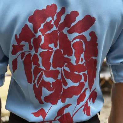 A close-up of the intricate hand-painted design on the back of our light blue shirt. This showcases the unique artistry and craftsmanship that goes into our one-of-a-kind pieces.