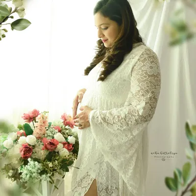 A serene moment by the window. The soft light, delicate white lace gown, and floral props create a dreamy and romantic boho-chic portrait.