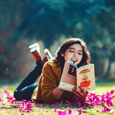 A candid portrait of a woman enjoying a book in the park. The low angle and scattered petals create a dreamy, peaceful atmosphere for this lifestyle photo.