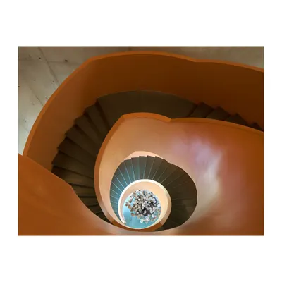An overhead view looking down a vibrant orange spiral staircase. This image captures how a staircase can become a powerful formal element, using geometry and color to create a dynamic spatial experience.