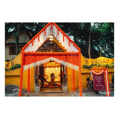 The entrance to a traditional naming ceremony at Ganjam Mantapa. The archway is heavily decorated with orange and white floral garlands, creating a grand and auspicious welcome.
