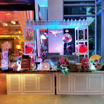 A whimsical and colorful Asian-themed food station designed for a corporate event at Hotel Andaz, New Delhi. The setup features decorative fans, umbrellas, and disco balls, creating a fun and memorable ambiance.