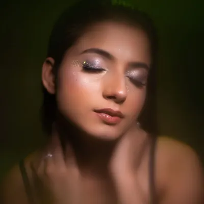 A dreamy beauty portrait with eyes closed to showcase the sparkling glitter eyeshadow. The soft, diffused lighting with a hint of green creates an ethereal and magical mood.