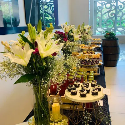 For a sophisticated event, I arranged this beautiful dessert and drinks table. The setup includes tall glass vases with fresh lilies and other flowers, adding a touch of elegance to the culinary display.