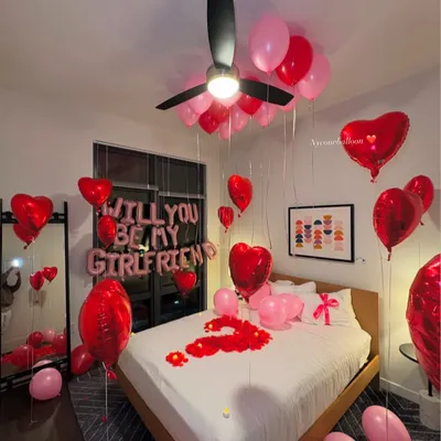 I can help you ask the big question with a beautiful surprise setup. This room features 'WILL YOU BE MY GIRLFRIEND' foil balloons, a mix of red and pink latex and heart-shaped foil balloons, and a bed covered in rose petals to create the perfect romantic proposal setting.