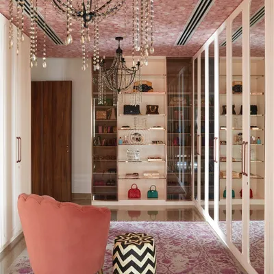 This walk-in wardrobe from our 'Palace in the Sky' project is pure luxury. We used soft pink hues, a wallpapered ceiling with crystal chandeliers, and custom shelving to display a stunning bag collection.