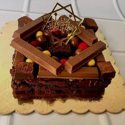 A side view of our overloaded brownie cake, showcasing its rich texture and generous toppings. This one is ready for a birthday celebration with a custom "Happy Birthday" topper.