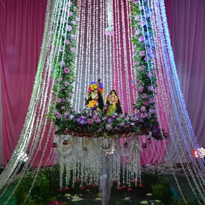 A divine swing setup for Radha and Krishna, decorated with an arch of fresh flowers and cascading strings of rajnigandha. The lighting adds a magical touch, making it a beautiful centerpiece for Janmashtami puja.