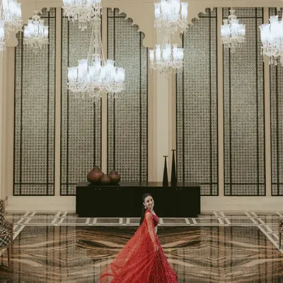 A breathtaking wide-angle portrait of the bride in a magnificent hall. The sweeping red lehenga, the grand chandeliers, and the opulent decor all combine to create a truly regal image.