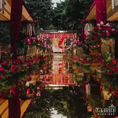The centerpiece of this South Indian decor was the stunning mirror glass aisle. It created a breathtaking reflection of the sky, the lush greenery, and the vibrant red floral arrangements, making the bride's walk feel like a journey through a floral wonderland.