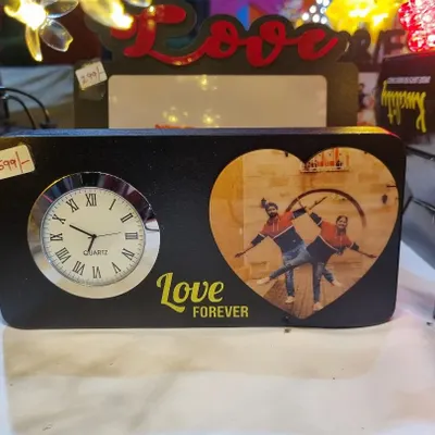 This tabletop clock is a sweet and personal gift. It features a classic analog clock face next to a heart-shaped frame for a personal photo, with the words "Love Forever" printed below.