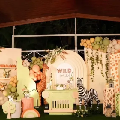 A grand "Wild One" jungle safari theme for a first birthday. This full-stage decoration includes multiple backdrops, custom arches, a dessert cart, and life-sized animal props like a zebra and elephant.