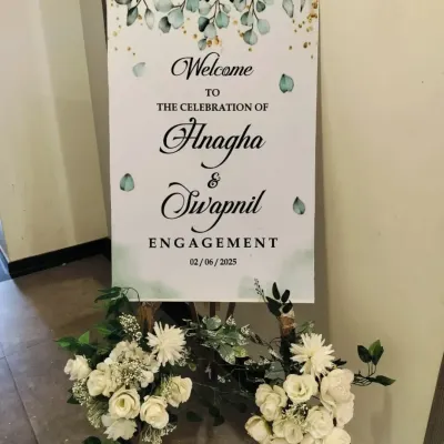 A personalized welcome sign for an engagement ceremony, placed on a wooden easel and decorated with white flowers. It's a simple touch that makes guests feel special.