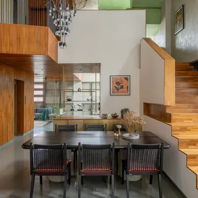This double-height dining area is defined by a dramatic, contemporary chandelier and warm wood paneling. The space opens up to a mezzanine level, creating visual connection across different floors of the home.