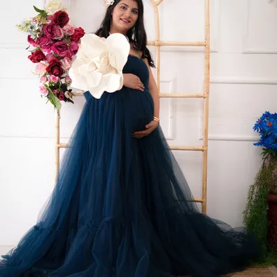 A solo portrait of the mother-to-be, radiating grace in a flowing teal gown. The floral arrangement and rustic ladder prop add a touch of elegance to this studio maternity session.