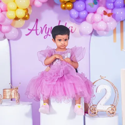 A sweet solo portrait of the birthday girl in her beautiful purple dress, set against the party's balloon decor.