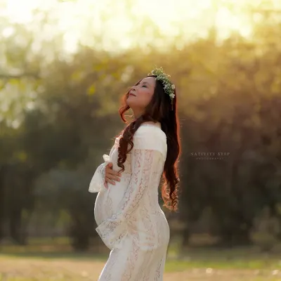 Soaking in the last rays of sun. This portrait in a white lace gown with a floral crown captures the pure, serene beauty of motherhood during the magical golden hour.
