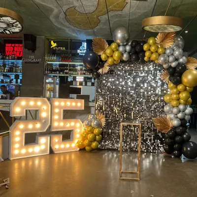 This setup for a 25th anniversary party features a full-size silver sequin wall that creates a dazzling effect. I paired it with large, illuminated marquee numbers and a balloon garland with gold, black, and silver chrome balloons for a truly celebratory feel.