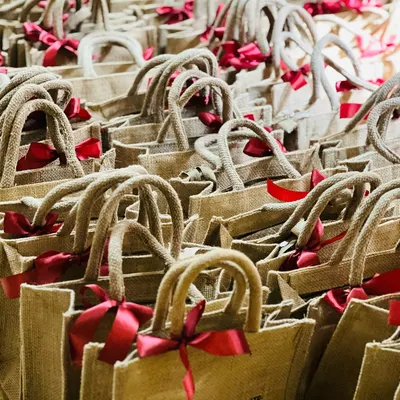 A large order of eco-friendly jute bags with rope handles and red ribbons, perfect for corporate event giveaways or welcome kits.