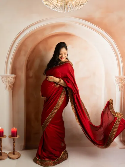 A smiling portrait with the red saree's pallu tossed gracefully. The warm lighting and classic backdrop create a celebratory mood.