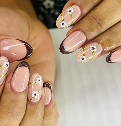 A lovely floral design with a modern twist. This set combines a classic brown French tip with accent nails featuring hand-painted daisies and crisscrossing gold lines.