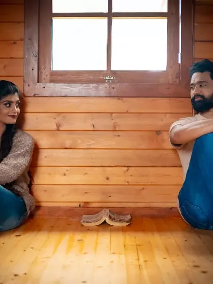 A relaxed portrait of a couple in a rustic, wood-paneled room. The warm lighting and casual poses create a feeling of comfort and easy companionship.