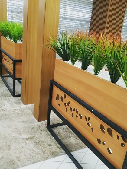 A close-up of the custom-designed planters for the restaurant. The warm wood box sits on a black metal frame with a decorative leaf-pattern cutout, adding a unique design detail that ties into the nature theme.